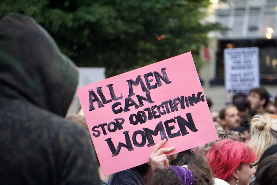 A group protest, with someone holding up a sign saying "All men can stop objectifying women"